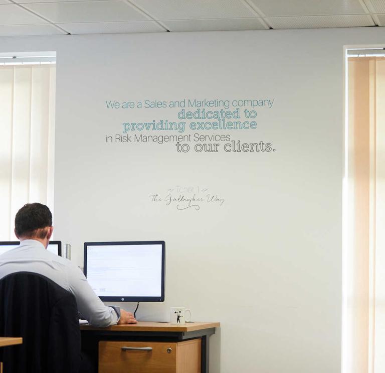 Man working in an office with slogan written on the wall above